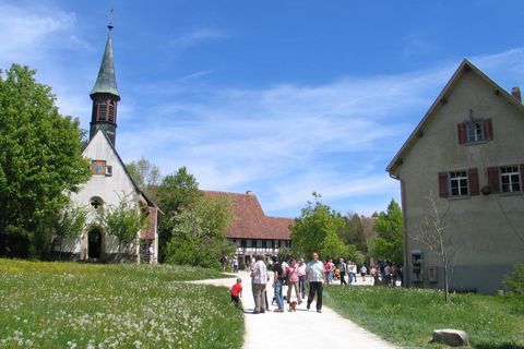 Das Freilichtmuseum Neuhausen ob Eck mit historischen Gebäuden wie z. B. einer Kirche und eines alten Wohngebäudes. Im Vordergrund des Bildes sind Besucher beim Rundgang auf dem Freigelände zu sehen (@ Freilichtmuseum Neuhausen ob Eck)