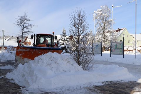 Hier sieht man ein Winterdienstfahrzeug der Gemeinde im Einsatz. Es wird gerade Schnee auf einem Platz geräumt. 