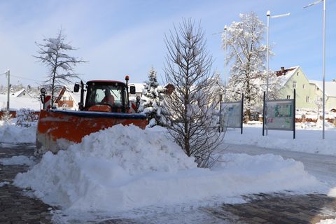 Hier sieht man ein Winterdienstfahrzeug der Gemeinde im Einsatz. Es wird gerade Schnee auf einem Platz geräumt. 