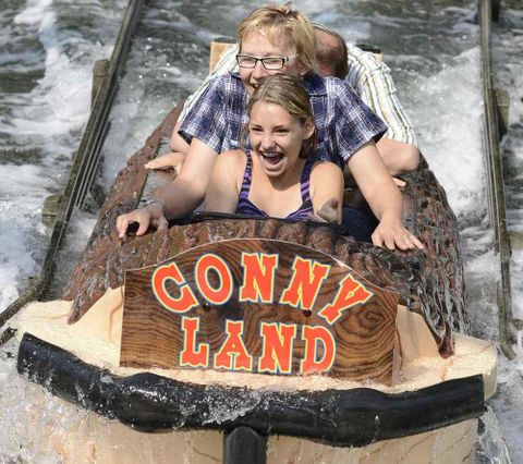 Ein Mädchen und eine Frau fahren sitzend in einem Baumstamm die Wildwasserbahn im Conny-Land