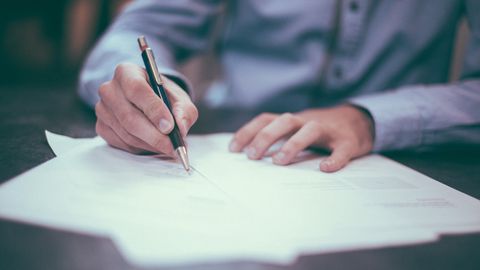 Eine Hand hält einen Stift in der Hand, der auf Papier schreibt.