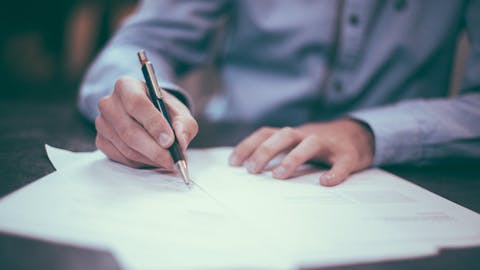 Eine Hand hält einen Stift in der Hand, der auf Papier schreibt.